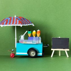 Ice cream toy cart with blue red umbrella. Assortment of ice cream empty menu black chalkboard.